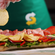 Subway employee sprinkling chips over sandwich